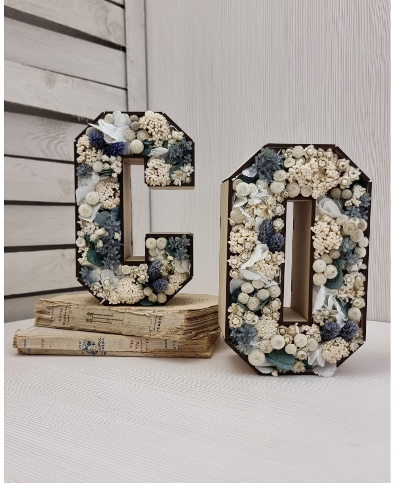 Letra decorativa con flores preservadas sobre base tipo libro.